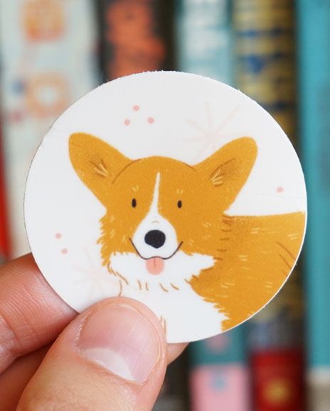 A hand holds a corgi sticker